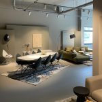 Showroom mit großen Tisch und 8 Stühlen, Teppichen, Stehlampen, Deko Stellwände und Sofa mit Kissen. Lichtsysteme an der Decken in der Rheinallee 56A, 55118 Mainz