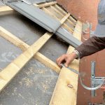 Bauarbeiter bringt Dachrinnen-Halter an die Holz Dachkonstruktion in der Dahlmannstraße. 58, 60385 Frankfurt am Main